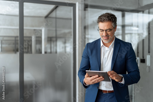 Executive man in suit working using computer for financial business banking work. Smiling senior mature Indian or Latin entrepreneur businessman looking at digital tablet screen in office. Copy space 