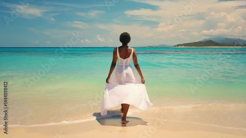 A young woman in a summer white dress walks on the sand of a tropical beach by the sea.