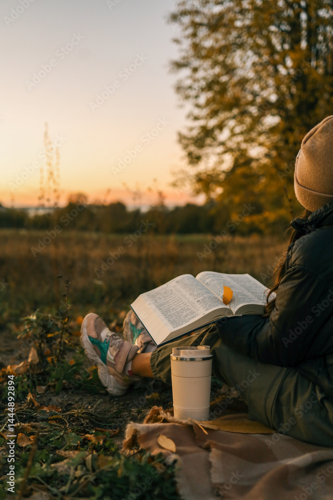 custom made wallpaper toronto digitalGirl reading book at sunset in autumn field. Bible open on her lap, reusable cup nearby, cozy mood with warm tones and falling leaf