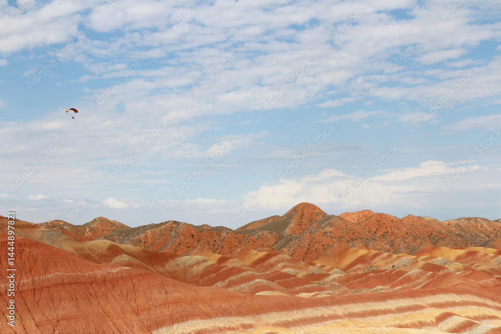 Fototapeta premium A paraglider flying against the blue sky with white clouds at Zhangye Danxia National Geopark (Rainbow Mountains) in Gansu, China