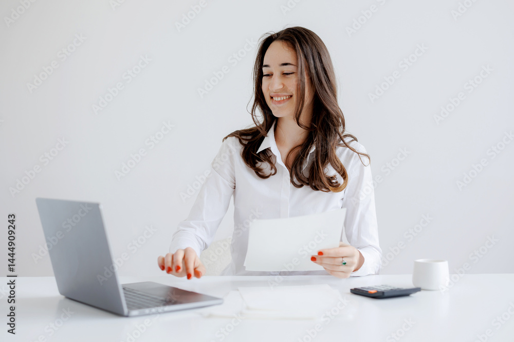Smiling woman working at her desk with a laptop and documents in a modern office setting