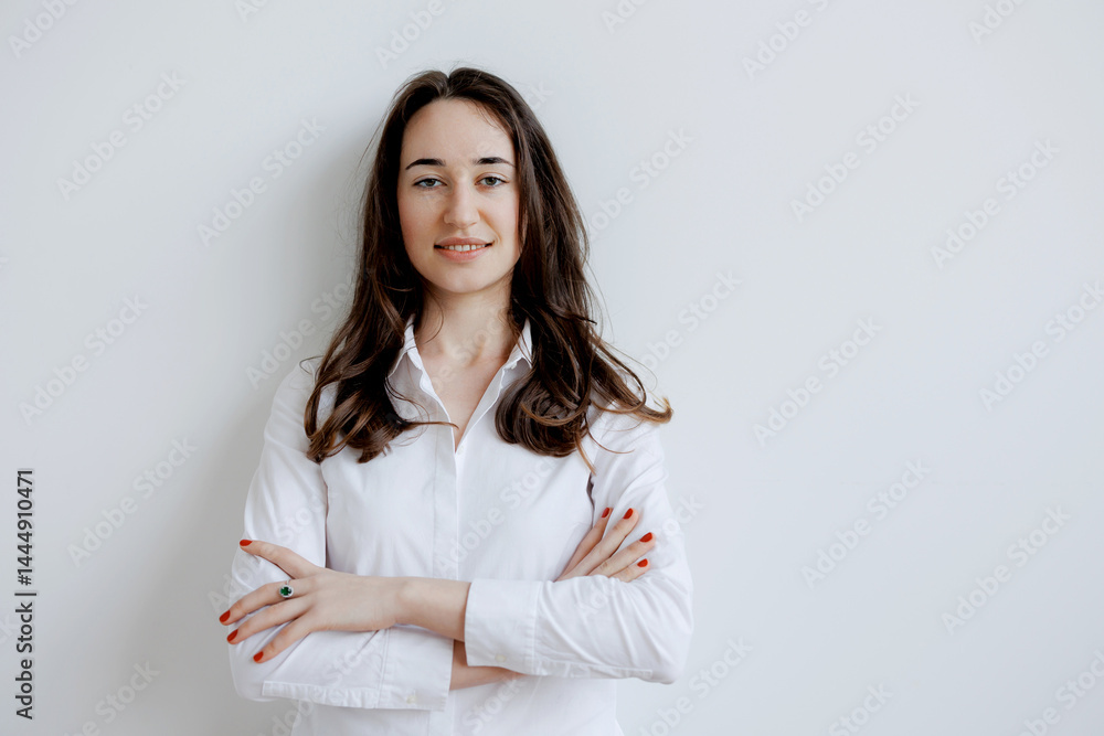 Confident woman in a white shirt standing against a plain wall with arms crossed
