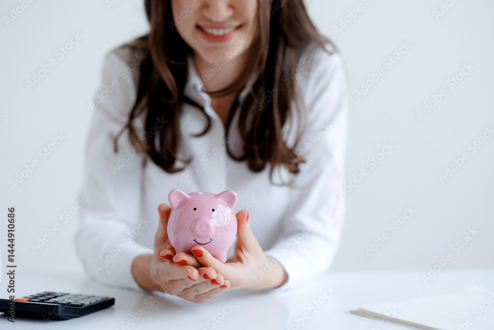 Woman holding a pink piggy bank at a desk during a financial planning session in a bright office environment