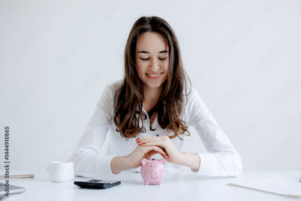 Young woman managing her finances with a piggy bank and calculator during a financial planning session at a bright workspace