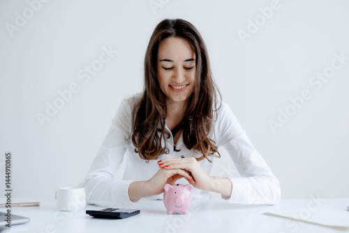 Obraz na płótnie Young woman managing her finances with a piggy bank and calculator during a financial planning session at a bright workspace w salonie