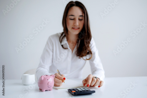 Obraz na płótnie Woman calculating expenses with a calculator and piggy bank on a desk in a bright office setting w salonie