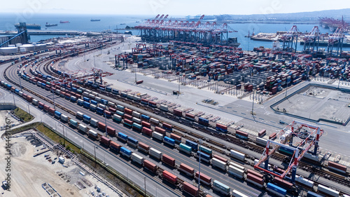 High-angle view of towering shipping cranes moving containers from a large cargo ship docked at a seaport. The deep blue ocean and colorful containers create a dynamic logistics scene.