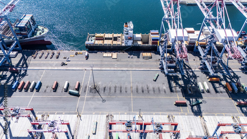 High-angle view of towering shipping cranes moving containers from a large cargo ship docked at a seaport. The deep blue ocean and colorful containers create a dynamic logistics scene.