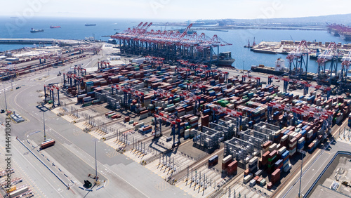 High-angle view of towering shipping cranes moving containers from a large cargo ship docked at a seaport. The deep blue ocean and colorful containers create a dynamic logistics scene.