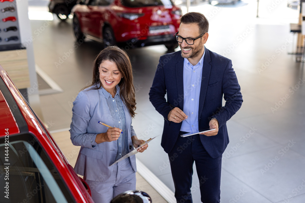 Super sales team in dealership, two consultants or managers in elegant suits with laptop and tablet in arms in car dealership Super sales team in dealership, two consultants or managers in elegant suits with laptop and tablet in arms in car dealership