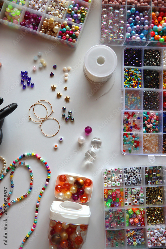Hand figurine, colorful friendship bracelets, necklaces, various beads and DIY supplies on the table. Making jewelry at home. Flat lay.