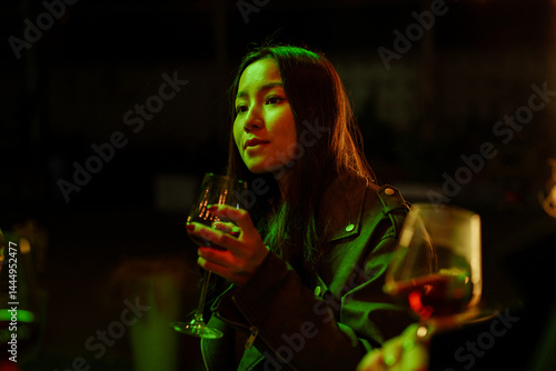 Obraz na płótnie Woman enjoying a drink during a lively gathering in a dimly lit setting with vibrant green lights at night w salonie