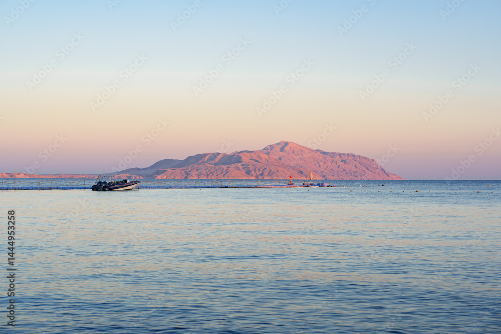 Sunrise casts soft hues over tranquil waters near desert island in early morning
