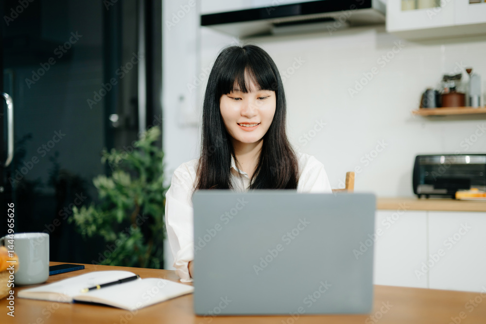 Asian woman working remotely on a laptop and tablet in a cozy kitchen workspace. Perfect for education, freelance Asian woman working remotely on a laptop and tablet in a cozy kitchen workspace. Perfect for education, freelance