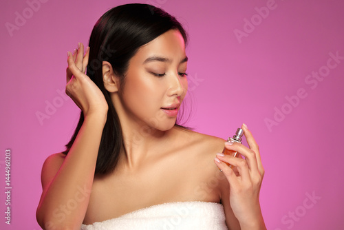 Obraz na płótnie Woman applying fragrance in a studio with pink background during a beauty session w salonie