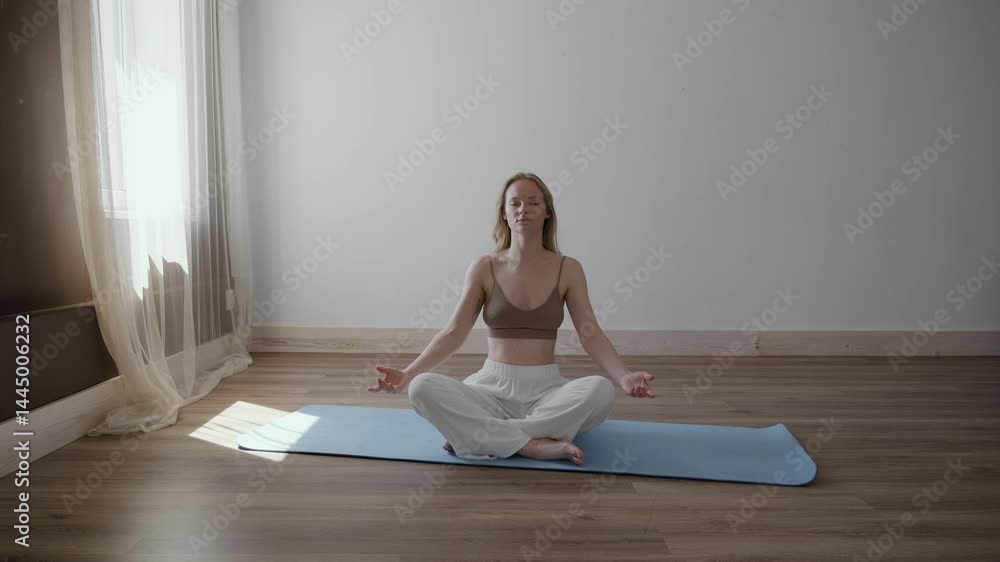 A young beautiful woman sits on a mat and meditates in a sunlit room. She gracefully performs yoga exercises, completely immersed in the moment. A young beautiful woman sits on a mat and meditates in a sunlit room. She gracefully performs yoga exercises, completely immersed in the moment.