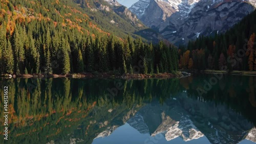 Serene alpine lake mirror reflection with autumn foliage and snow-capped mountains
