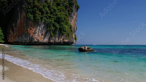Turquoise tropical beach with white sand and towering limestone cliffs
