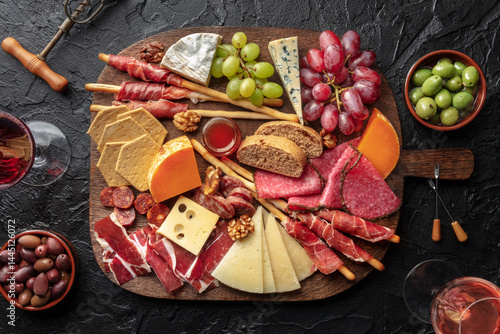 Antipasti or tapas. Charcuterie and cheese platter with wine, shot from above on a black table. Italian or Spanish food and drinks