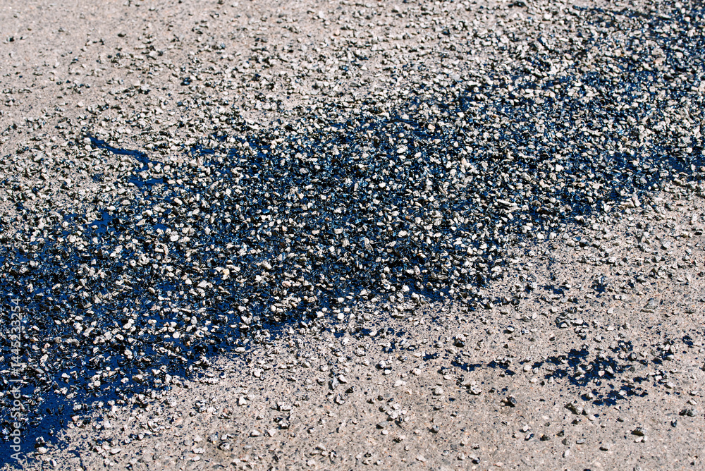 Asphalt surface repair with fresh bitumen patch and resin treatment applied to cracked pavement, urban road maintenance. Patchwork using hot bitumen, gravel, and resin coating to seal road cracks