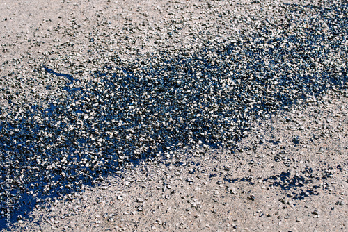 Asphalt surface repair with fresh bitumen patch and resin treatment applied to cracked pavement, urban road maintenance. Patchwork using hot bitumen, gravel, and resin coating to seal road cracks