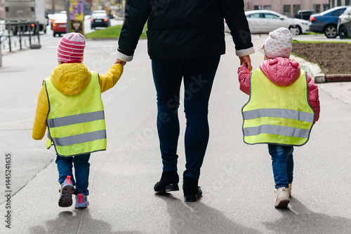 Bilde på lerret Two young girls in protective reflective vests walk with their mother by hands a
