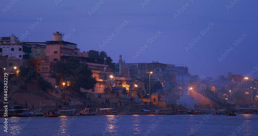 Varanasi, Uttar Pradesh, India. People walking on steps on Shivala Ghat and floating in boats near Dandi Ghat. Evening time. Camera moving along riverbank embankment. Cinematic View from river