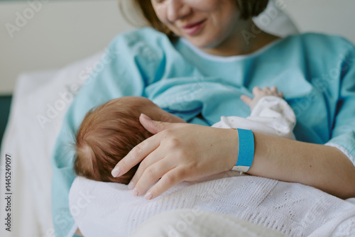 Foto New mother in hospital gown breastfeeding newborn baby while holding closely