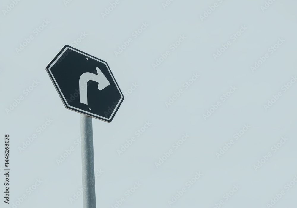 A black hexagonal direction sign showing a white right turn arrow against a pale sky. Road safety concept and travel planning for traffic guidance.