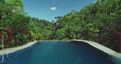 Luxury infinity swimming pool overlooks a vibrant tropical jungle valley forest, offering breathtaking views of nature beauty and creating a serene escape. Exotic travel vacation getaway. Drone flight