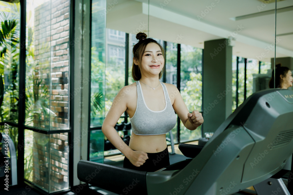 A young woman enjoys a light cardio jog on the treadmill at the gym, headphones on and music playing as she stays focused and relaxed.