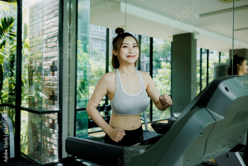 Obraz na płótnie A young woman enjoys a light cardio jog on the treadmill at the gym, headphones on and music playing as she stays focused and relaxed. w salonie