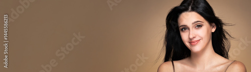Banner with beauty studio portrait of young beautiful smiling woman with black loose waving hair against beige background