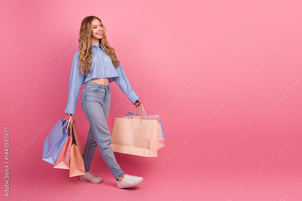 Stylish young woman carrying multiple shopping bags on pastel pink background exuding happiness and charm