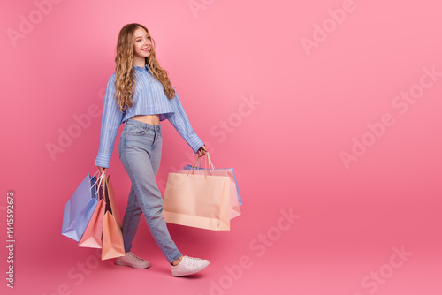 Obraz na płótnie Stylish young woman carrying multiple shopping bags on pastel pink background exuding happiness and charm w salonie