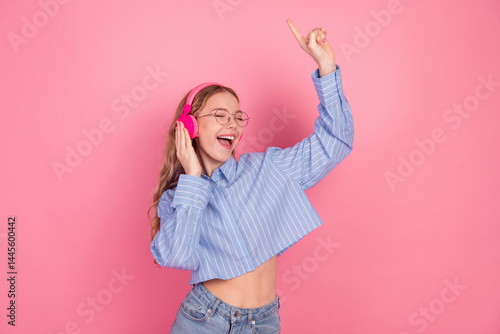 Obraz na płótnie Young joyful woman in stylish attire enjoying music with headphones against a pink background expressing happiness and leisure w salonie