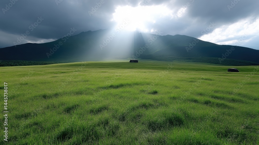 Lush green meadow stretches under dramatic sky with mountain backdrop and sunbeams Lush green meadow stretches under dramatic sky with mountain backdrop and sunbeams