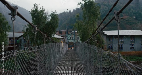 Suspension bridge in a village in Nepal, surrounded by mountains, perfect for travel brochures, websites, and social media posts.
