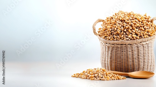 A close-up shot of a woven bag overflowing with barley grains, with a wooden spoon beside it, placed on a smooth, neutral surface.