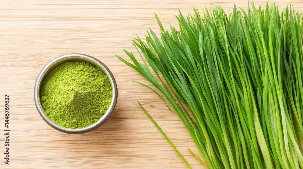 A close-up shot of wheatgrass powder in a small bowl, with raw wheatgrass stalks laid out beside it on a wooden surface.
