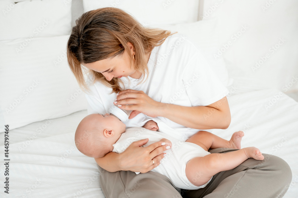 mom feeds the baby with a bottle of milk or formula, feeding the baby in her arms, a young mother feeds the newborn baby at home on the bed mom feeds the baby with a bottle of milk or formula, feeding the baby in her arms, a young mother feeds the newborn baby at home on the bed