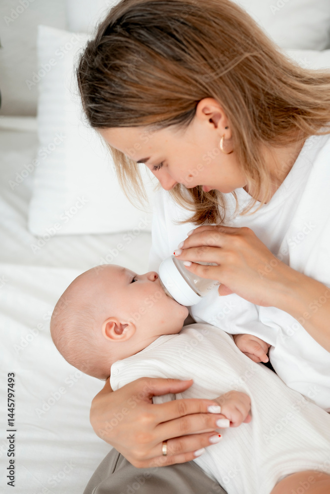 mom feeds the baby with a bottle of milk or formula, feeding the baby in her arms, a young mother feeds the newborn baby at home on the bed mom feeds the baby with a bottle of milk or formula, feeding the baby in her arms, a young mother feeds the newborn baby at home on the bed