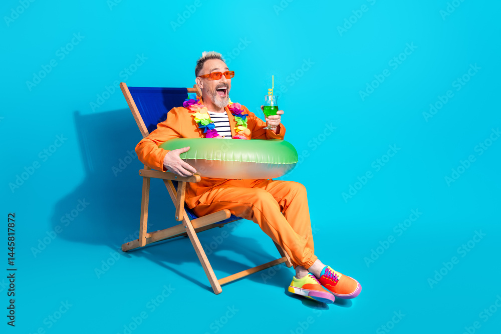 Middle aged man in orange suit enjoying summer vibe with tropical drink against blue background featuring leisure and style