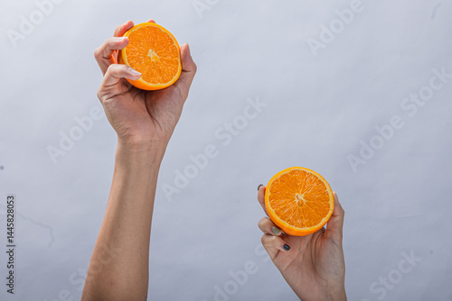 Two hands holding fresh orange halves against a plain light background, showing juicy citrus texture, vibrant color, and a healthy, natural fruit presentation in midair pose