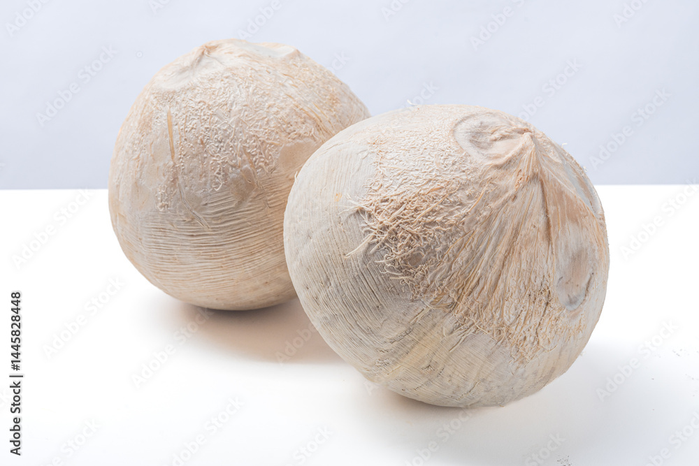 Two peeled young coconuts placed on a clean white surface with soft background, showing rough fibrous texture, tropical freshness, and natural appearance of healthy exotic fruit Two peeled young coconuts placed on a clean white surface with soft background, showing rough fibrous texture, tropical freshness, and natural appearance of healthy exotic fruit