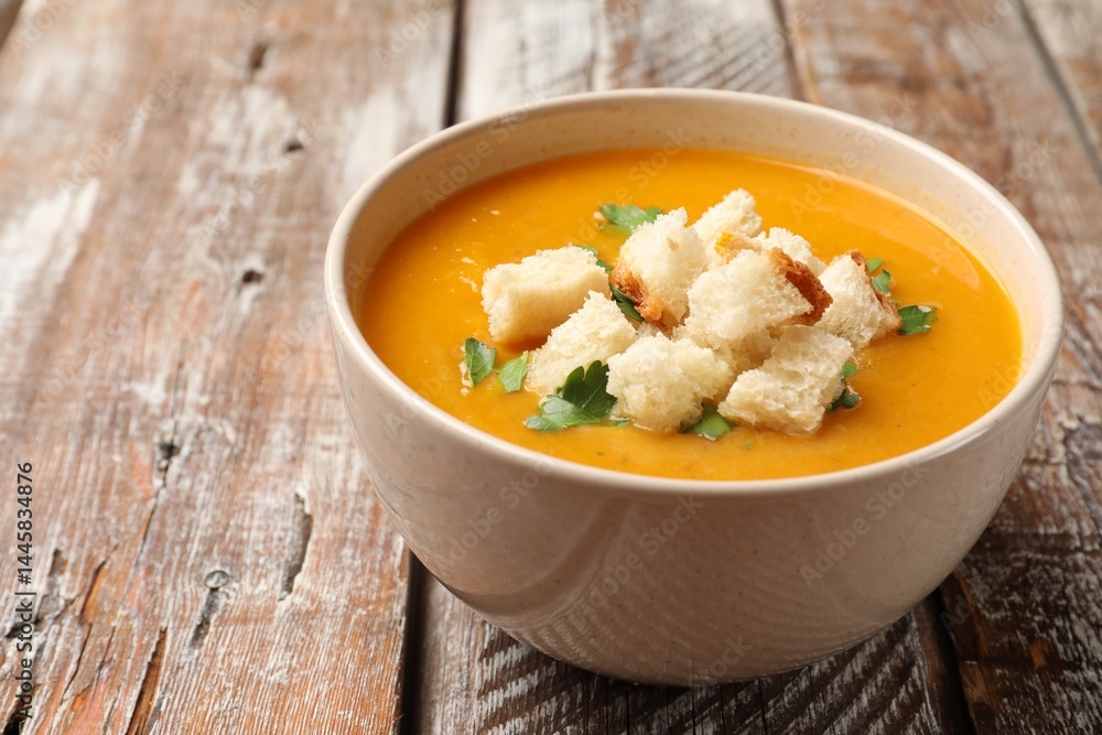 Tasty pumpkin cream soup with croutons and parsley in bowl on wooden table, closeup. Space for text Tasty pumpkin cream soup with croutons and parsley in bowl on wooden table, closeup. Space for text
