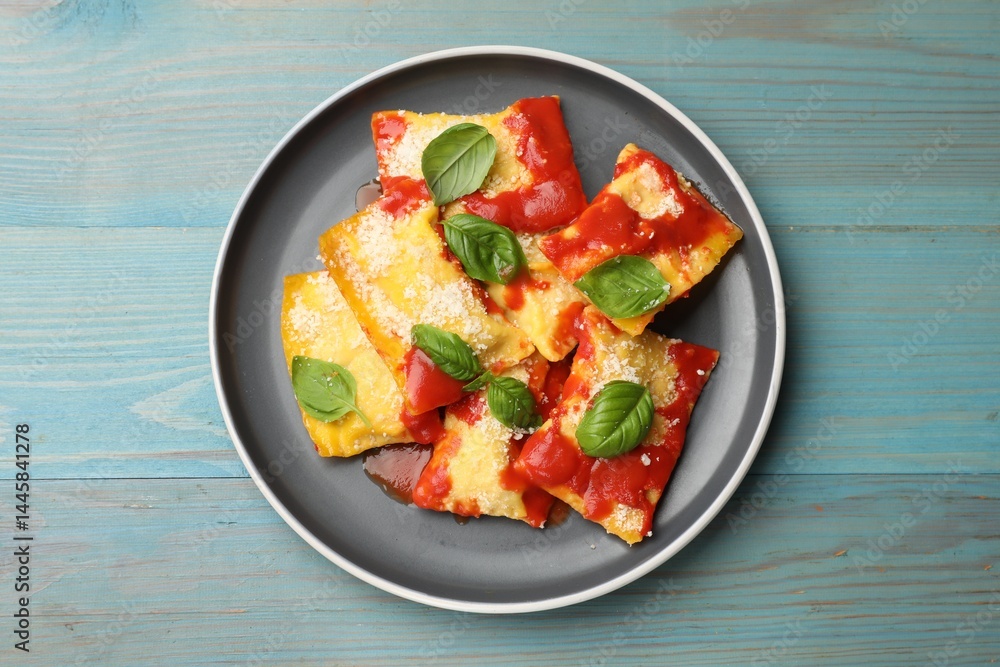 Delicious ravioli with tomato sauce, parmesan cheese and basil on blue wooden table, top view Delicious ravioli with tomato sauce, parmesan cheese and basil on blue wooden table, top view