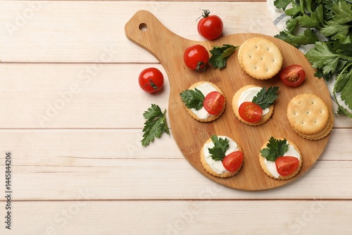 Tasty crackers with cream cheese, tomatoes and parsley on white wooden table, flat lay. Space for text