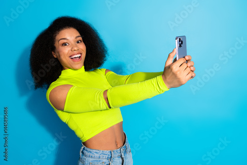 Smiling woman taking a selfie in a vibrant neon outfit on blue background, conveying youth, happiness, and style