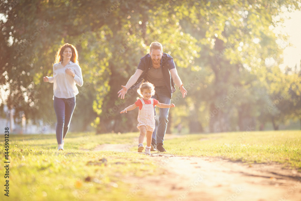 Naklejka premium Young happy parents with their baby girl having fun outdoors